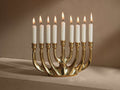 Front view of the polished brass Sculptural Menorah with nine lit white taper candles.