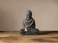 Seated Buddha statue made of dark gray cast stone with a natural finish, wearing light wood prayer beads and tassel.