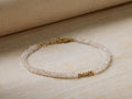 Selah Bracelet with faceted clear zircon beads, gold vermeil clasp, and three gold accent beads on cream fabric.