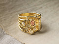Top view of a gold-toned Serina Ring with multiple bands, twisted rope texture, oval reddish-brown inlay, and clear round stones.