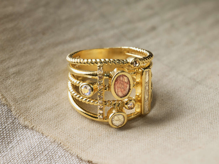 Top view of a gold-toned Serina Ring with multiple bands, twisted rope texture, oval reddish-brown inlay, and clear round stones.