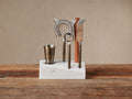Sienna Bar Tool Set: Antiqued brass steel tools & wood muddler in white marble stand on a wooden table.