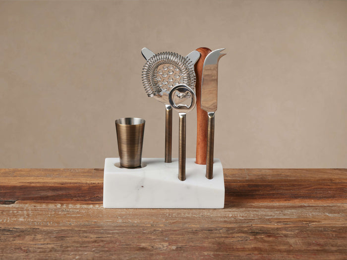 Sienna Bar Tool Set: Antiqued brass steel tools & wood muddler in white marble stand on a wooden table.