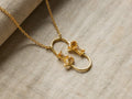 Sienna Citrine Necklace: Gold chain, central pendant with two interconnected loops, each holding two golden citrine stones, on light fabric.