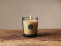 Lit Signature Candle in Lemon Blackberry and Cassis. Yellow wax in tinted glass with a dark embossed label on rustic wood.