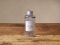 Clear glass Arhaus Signature Lemon Diffuser Refill bottle with silver cap & 'Lemon Blackberry & Cassis' label on wood.