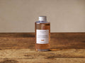 Arhaus Sandalwood Leaf & Tobacco diffuser refill: clear bottle with silver cap, amber oil, white label on rustic wood.