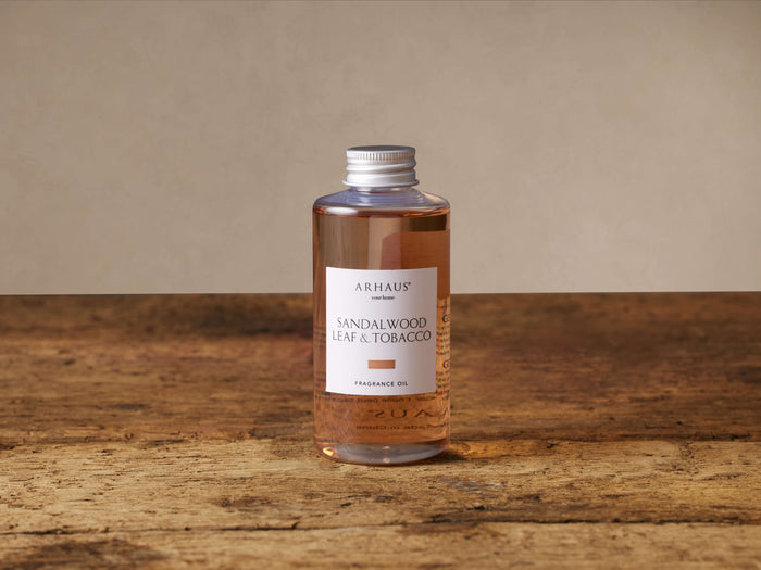 Arhaus Sandalwood Leaf & Tobacco diffuser refill: clear bottle with silver cap, amber oil, white label on rustic wood.