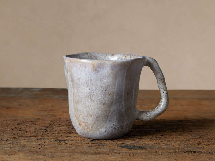Skye Mug: handcrafted, organically shaped stoneware mug with unique reactive white glaze, subtle dark accents, on a rustic wood surface.