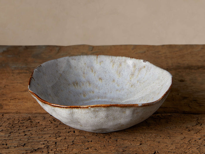 Handcrafted Skye Pasta Bowl, white stoneware with a transparent reactive glaze, subtle patterns, and a dark brown rim on rustic wood.