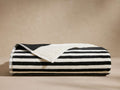 Folded Solara Beach Towel displaying bold black and white cabana stripes. Plush texture visible, with a corner slightly unfolded.