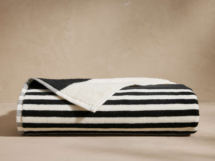 Folded Solara Beach Towel displaying bold black and white cabana stripes. Plush texture visible, with a corner slightly unfolded.