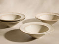 Speckled ivory Solenne Cereal Bowls (Set of 4) with glossy finish and exaggerated rims, two bowls stacked on left.
