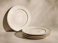 Arrangement of four cream round dinner plates with brown speckles. One stands upright, three are stacked horizontally.