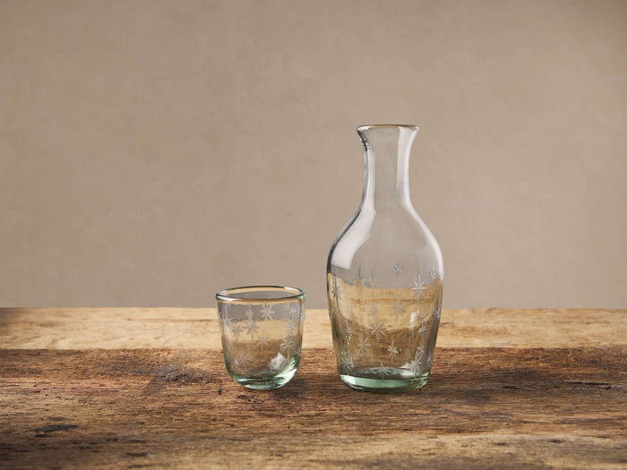 Green-tinted Star Bedside Carafe & glass with etched stars, standing upright on a textured wooden table.