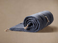 Muted blue Stone Washed Velvet Throwbed, partially rolled, with a cream strap and jute tassels, on a beige background.