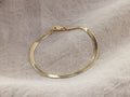Sura Snake Chain Bracelet in gold vermeil, lying on beige fabric. Features a flat, gleaming design with a secure clasp.