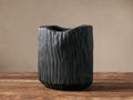 Black, hand-carved Surma Vase with organic, wavy top and textured, bark-like surface, standing on a wooden table.