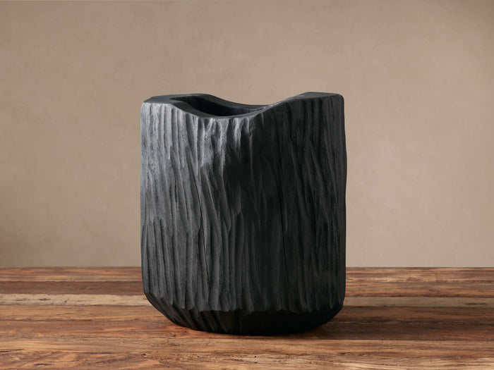 Black, hand-carved Surma Vase with organic, wavy top and textured, bark-like surface, standing on a wooden table.