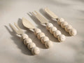 Angled view of four beige and ivory Sylvaine Cheese Knives, two forked and two spade-like, with spherical travertine handles.