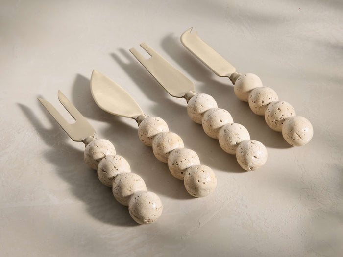 Angled view of four beige and ivory Sylvaine Cheese Knives, two forked and two spade-like, with spherical travertine handles.