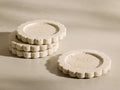 Front view of three stacked and one separate beige and ivory-toned natural travertine Sylvaine Coasters with scalloped edges.