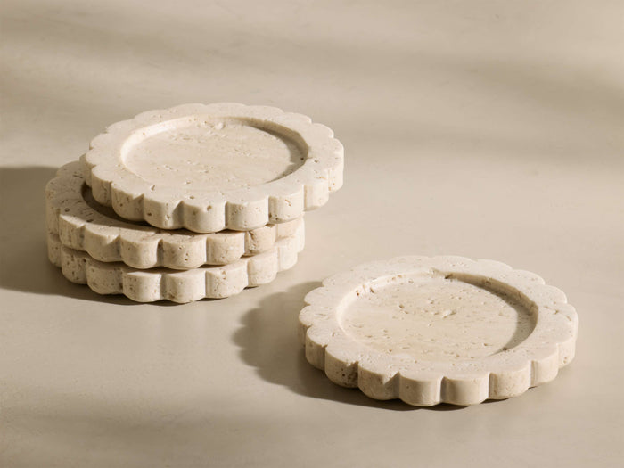 Front view of three stacked and one separate beige and ivory-toned natural travertine Sylvaine Coasters with scalloped edges.