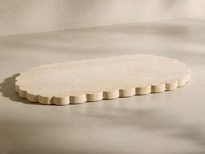 Angled view of the beige and ivory-toned travertine Sylvaine Oval Board, featuring scalloped edges and visible stone texture.