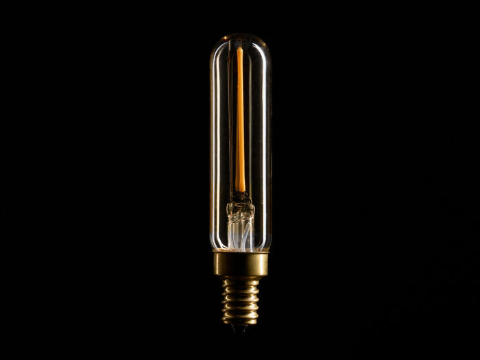 A tubular LED filament bulb with a clear glass casing and a brass base, illuminated against a black background.