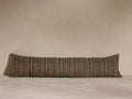 Long, textured bolster pillow with a brown and black woven pattern, set against a neutral-toned background on a flat surface.