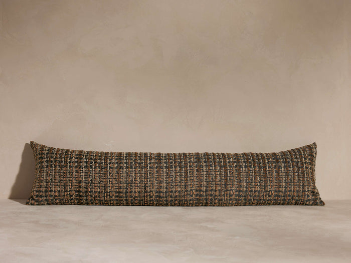 Long, textured bolster pillow with a brown and black woven pattern, set against a neutral-toned background on a flat surface.