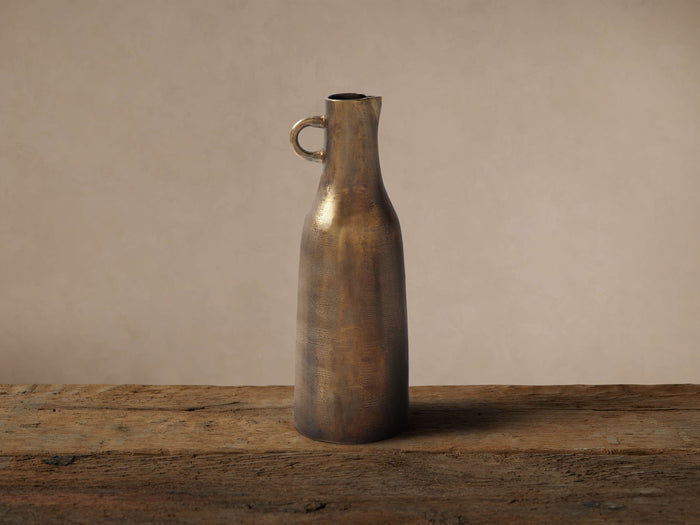 Taddeo Tall Jug, cast aluminum with an antique brass finish, featuring a C-handle, on a rustic wood surface.