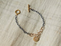 Yellow bronze Tavi bracelet with white diamond charm. Oxidized silver chain, gold-fill links, toggle clasp, on a fabric surface.