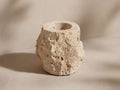 Natural, light beige travertine bath tumbler with rough, porous exterior and chiseled edges, standing upright on a pale surface.