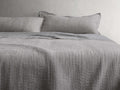 Tulaya Cotton Quilt on a bed with matching pillows, showcasing a textured, soft gray surface with frayed edges, suggesting comfort.