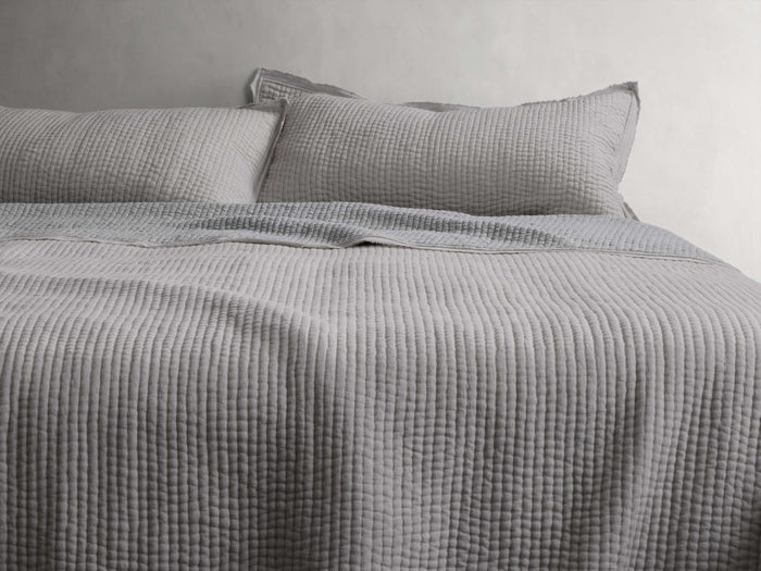 Tulaya Cotton Quilt on a bed with matching pillows, showcasing a textured, soft gray surface with frayed edges, suggesting comfort.