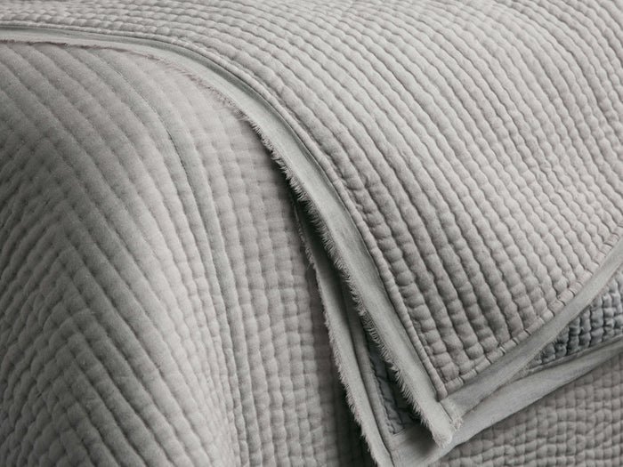 Close-up of a soft grey Tulaya Cotton Quilt with vertical quilting stitches and a detailed frayed edge.