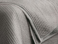 Close-up of a light gray Tulaya Cotton Quilt, folded with parallel stitching, showing the soft texture and frayed edge detail.