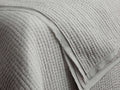 Close-up of a folded light grey Tulaya Cotton Quilt with parallel stitched channels and a soft, slightly frayed edge.