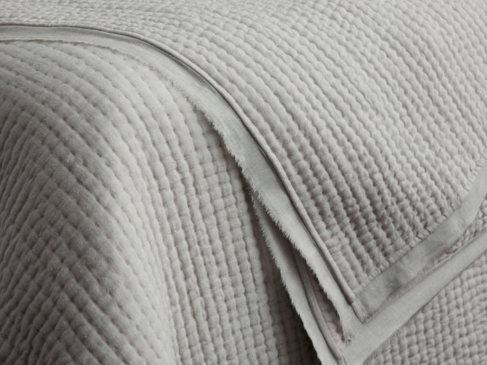 Close-up of a folded light grey Tulaya Cotton Quilt with parallel stitched channels and a soft, slightly frayed edge.