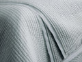 Close-up of a light sage green Tulaya Cotton Quilt, showcasing its soft, channel-quilted texture and frayed edges.