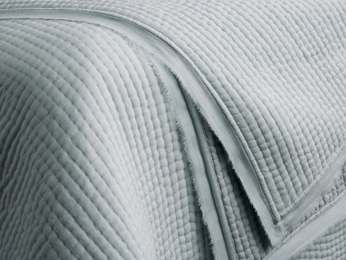 Close-up of a light sage green Tulaya Cotton Quilt, showcasing its soft, channel-quilted texture and frayed edges.