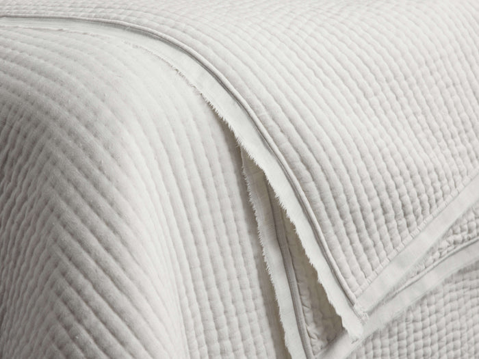 Close-up of a light gray Tulaya Cotton Quilt, showing its soft, quilted texture with parallel stitching and a frayed edge.