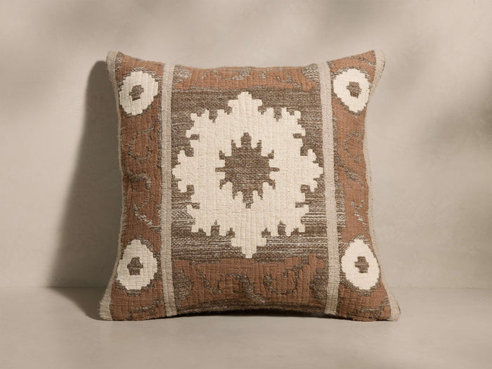 Front view of a square terracotta cushion with a large white geometric star and smaller corner motifs, bordered by taupe stripes.
