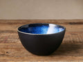 Twilight Cereal Bowl with deep blue reactive glaze interior and matte dark exterior on a rustic wooden table.