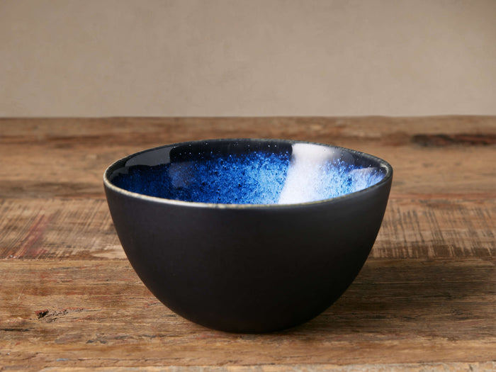 Twilight Cereal Bowl with deep blue reactive glaze interior and matte dark exterior on a rustic wooden table.