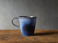 Twilight Mug in deep indigo stoneware with reactive glaze, subtle color variations, curved handle, on wooden surface.