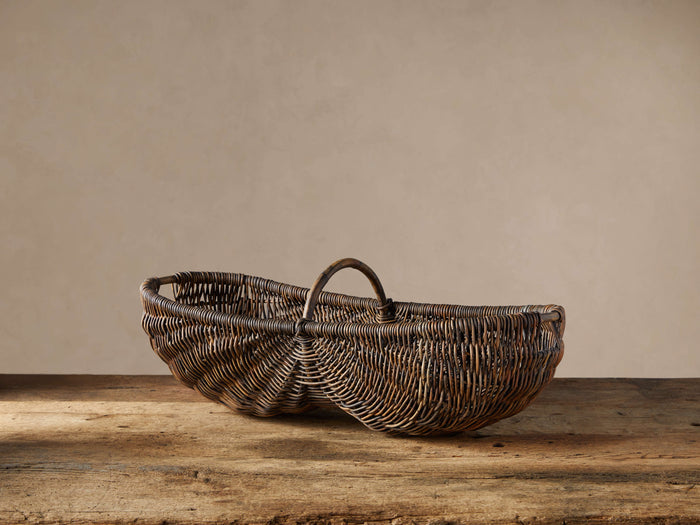 Handwoven vintage-stained arurog reed basket with a handle, resting on a rustic wooden surface against a light wall.