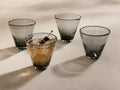 Four smoke Vireo Double Old Fashioned Glasses (Set of 4) with tapered bases, one with a drink, ice, and two cherries.