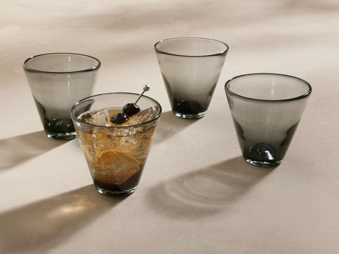 Four smoke Vireo Double Old Fashioned Glasses (Set of 4) with tapered bases, one with a drink, ice, and two cherries.